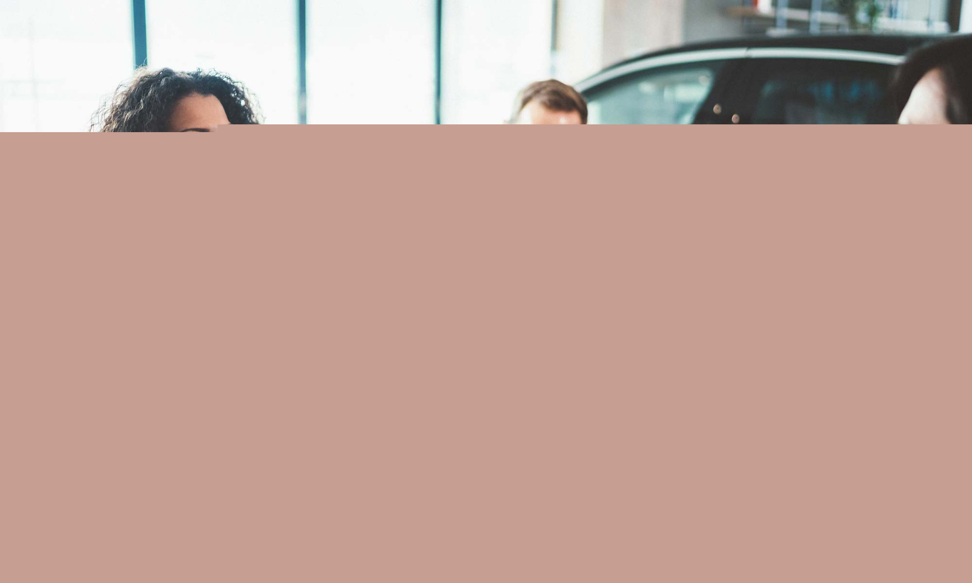 A couple handing over paper work to a salesman at a car dealership.